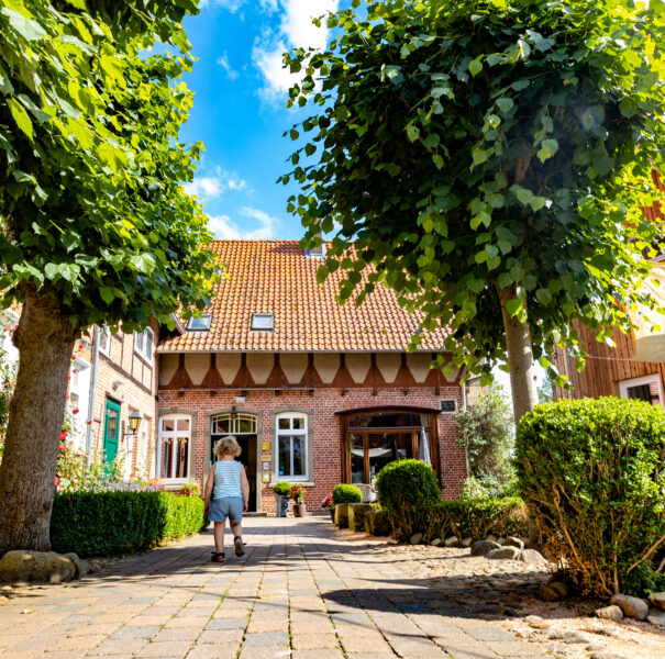 Die Außenfassade des Landhotels bei Sonnenschein, davor läuft ein kleines Kind