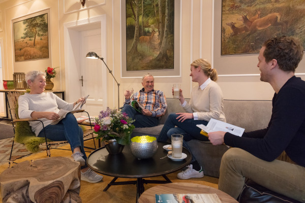 Vier Gäste sitzen in der Lobby, lesen Zeitschriften und trinken Kaffee