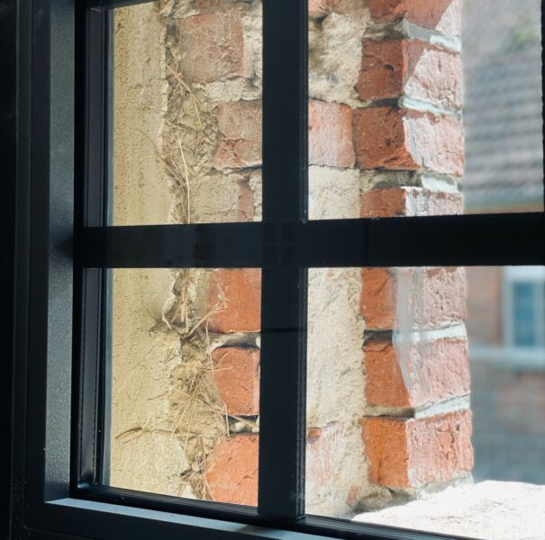 Blick aus einem schwarzen Fenster auf eine Ziegelwand