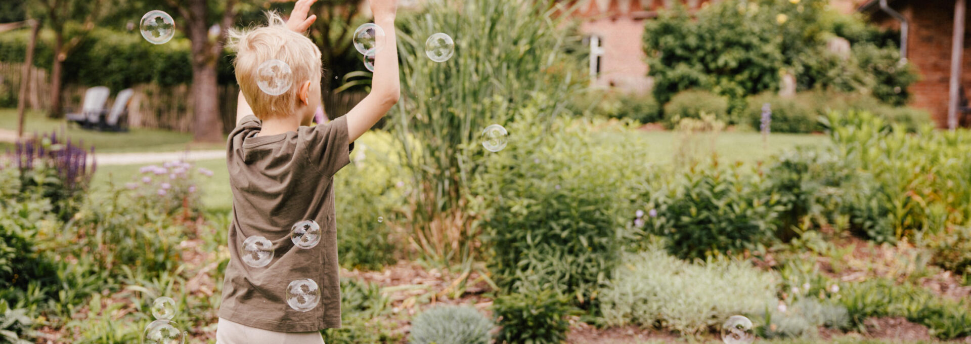 Kind fängt Seifenblasen auf Wiese vorm Bauernhaus