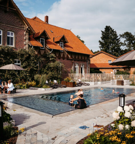 Eine Aufnahme des Außenpools des Landhotels mit mehreren Familien, großen Sonnenliegen und schönen Blumen.
