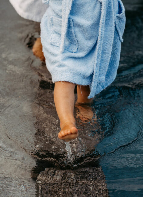 Kleine Babybeine sind in einen Bademantel gehüllt und spielen im Wasser