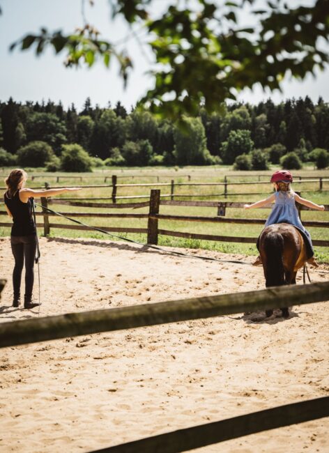 Reitlehrerin leitet ein kleines Mädchen, das auf einem Pony sitzt auf dem Reitplatz im Familienhotel Niedersachsen