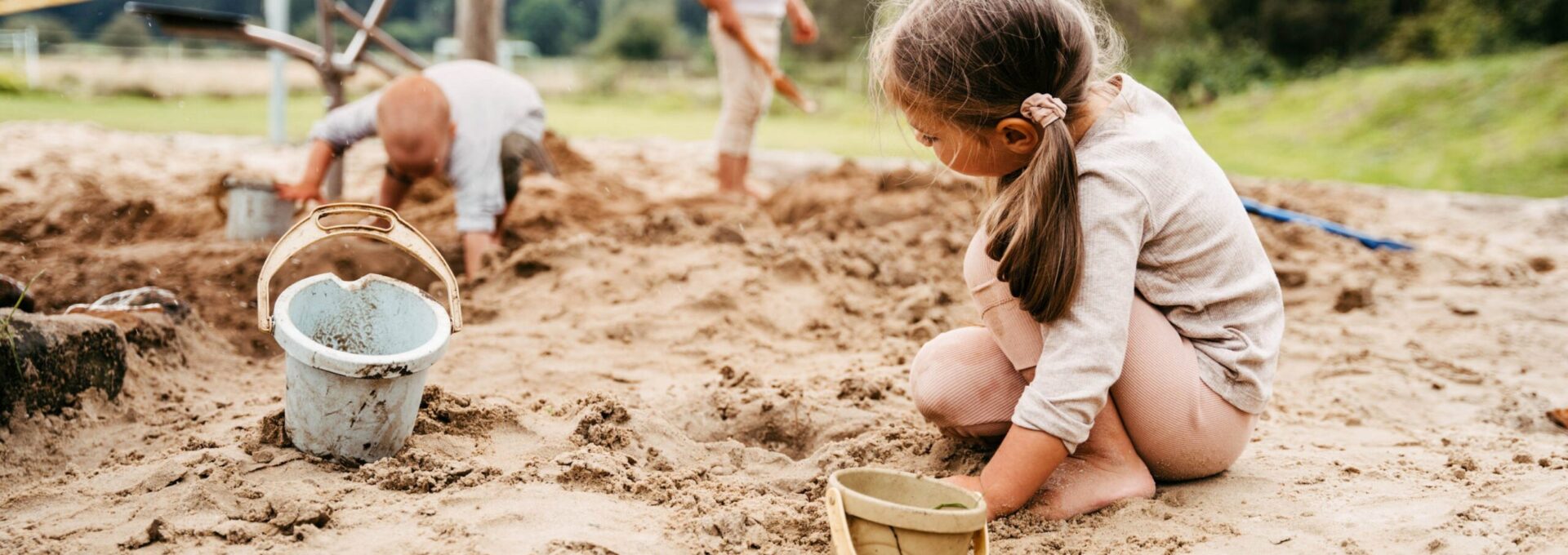 Drei Kinder spielen mit Eimern im Sandkasten im Hotel mit Kinderbetreuung
