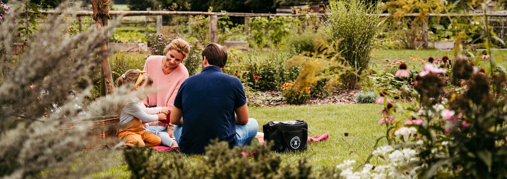 Eine Familie sitzt im Freien und picknickt auf einer roten Decke mit Picknickkorb.