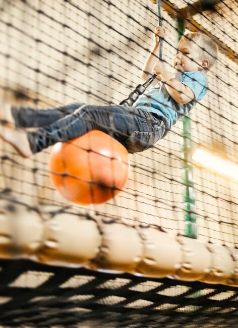 Ein kleiner Junge schwingt an einem Seil in der Spielscheunen beim All inclusive Familienurlaub