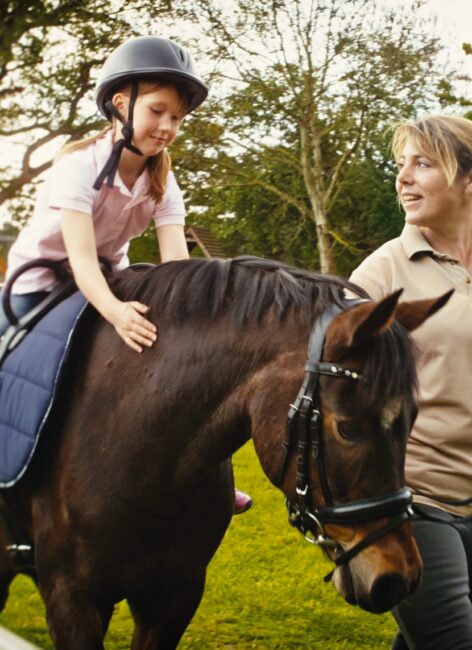Reitlehrerin leitet ein kleines Mädchen, das auf einem Pferd reitet beim all inclusive Familienurlaub