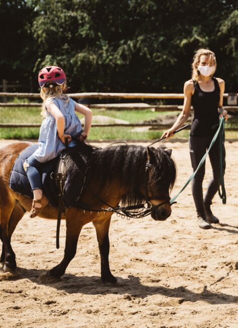 Reitlehrerin leitet ein kleines Mädchen, das rückwärts auf einem Pony sitzt beim all inclusive Familienurlaub