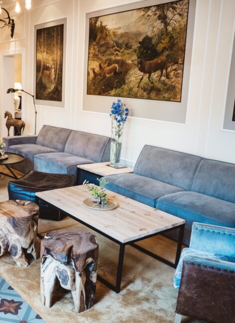 Blick in die Lobby mit gemütlichen, blauen Sofas und Hockern aus Holz im Kinderhotel mit Schwimmbad