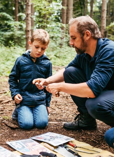 Ein Kind und ein Mann sitzen auf dem Waldboden und schauen sich Werkzeuge an nahe dem Hotel mit Kinderbetreuung