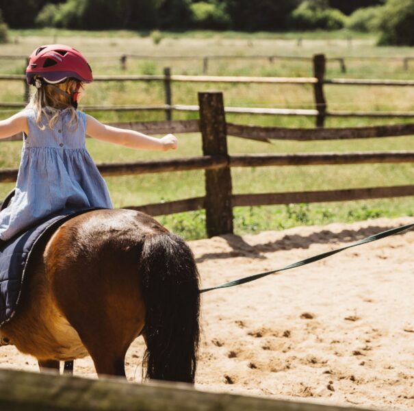 Kleines Mädchen sitzt auf einem Pony und streckt beide Arme zur Seite aus.