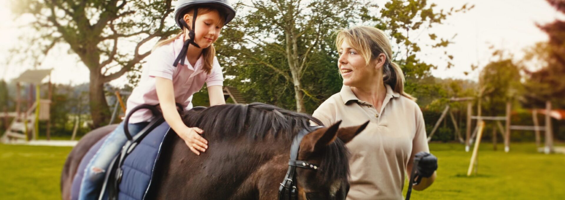Kleines Mädchen sitzt auf einem Pferd, das von einer Reitlehrerin geführt wird