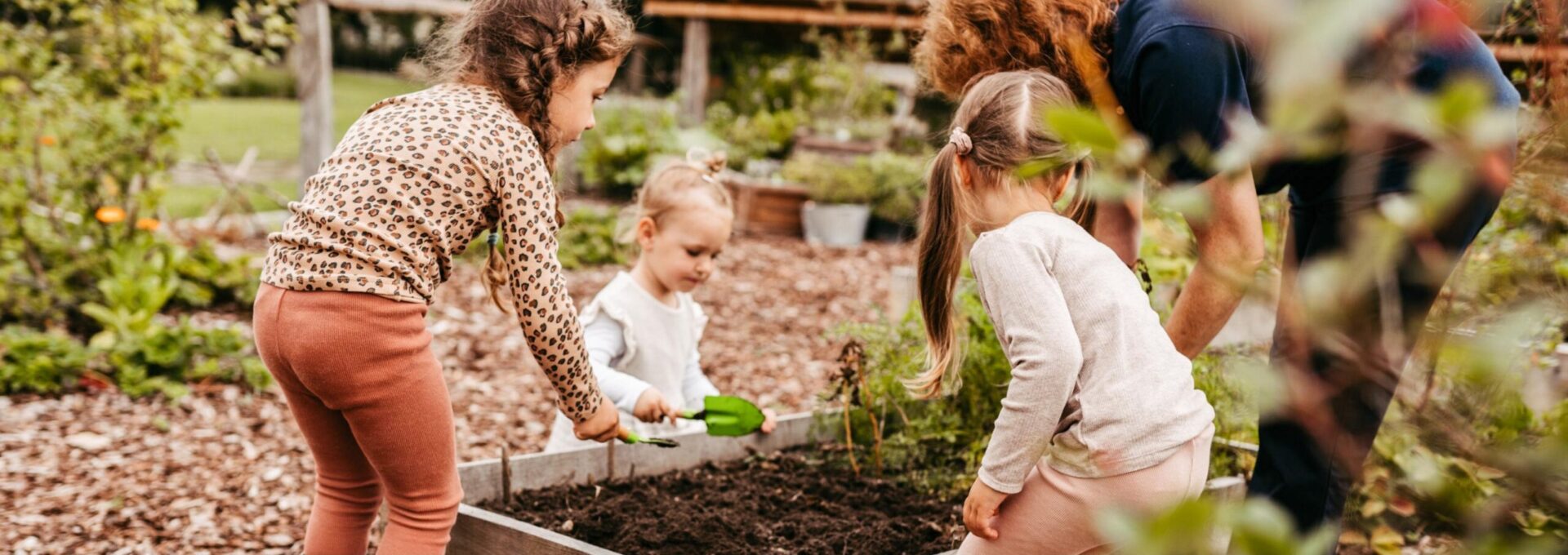 Drei kleine Mädchen gärtnern gemeinsam mit einer Mitarbeiterin in einem Beet im Landhaus Averbeck