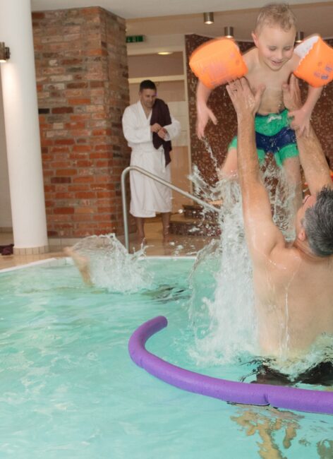 Detailaufnahme eines Vaters und Sohnes spielend im Pool während Ihres All Inclusive Familienurlaubs.