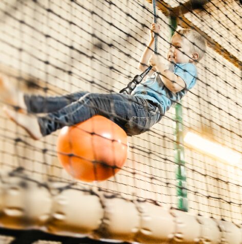 Junge hängt an einem Seil und sitzt auf einem Ball im Familienhotel und Bauernhof Averbeck.