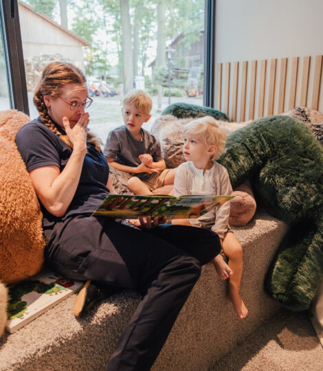 Kinderbetreuerin liest in einer Kuschelecke Kindern ein Buch vor