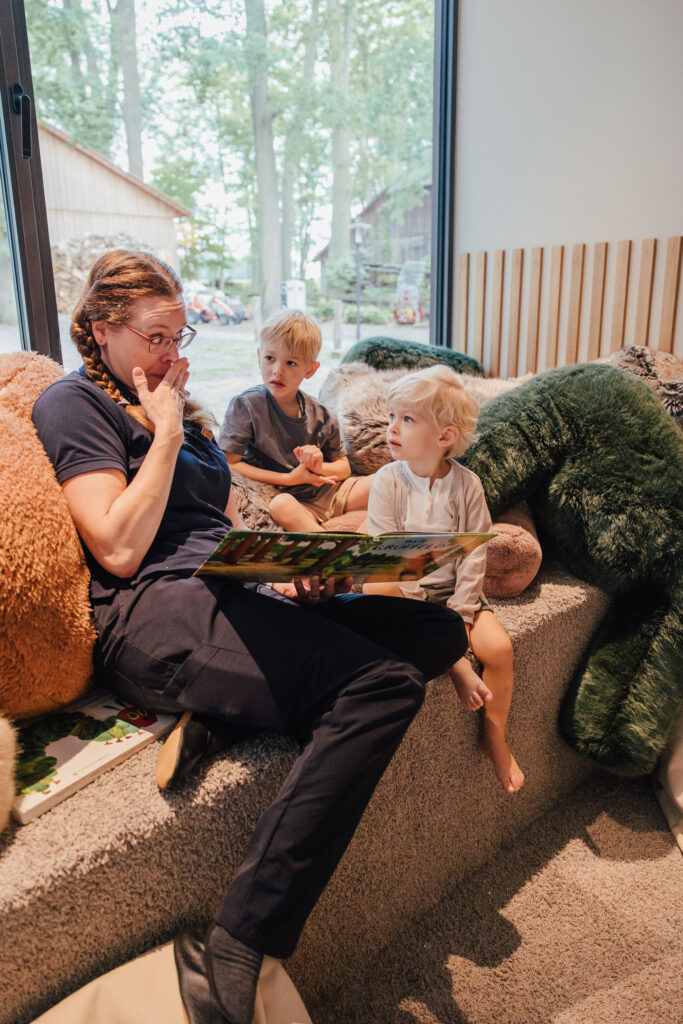 Kinderbetreuerin liest in einer Kuschelecke Kindern ein Buch vor