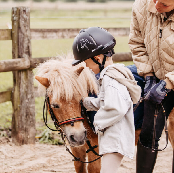 Junge streichelt ein Pony mit der Reitlehrerin.