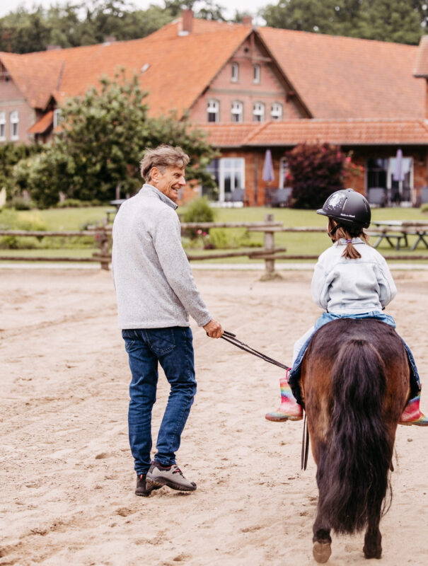 Opa führt seine Enkeltochter auf einem Reitplatz auf einem Pony.