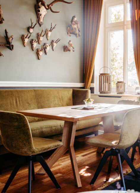 Tisch mit Sitzbank und Stühlen mit Jagdtrophäen an der Wand im Familienhotel mit Bauernhof