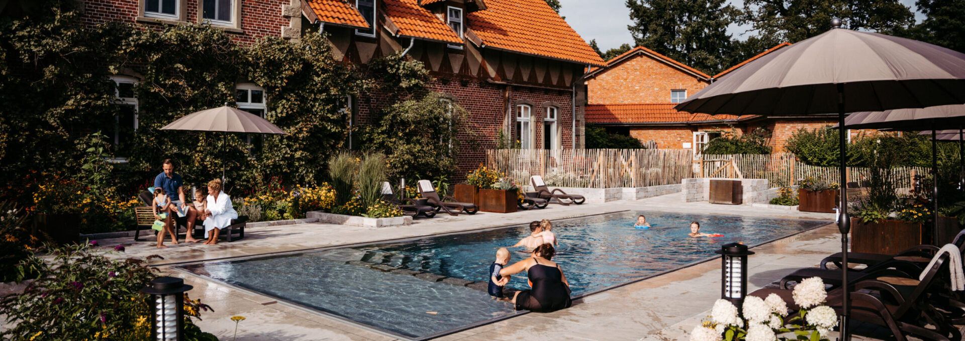 Familien sitzen am Außenpool und schwimmen im Familienhotel mit Bauernhof