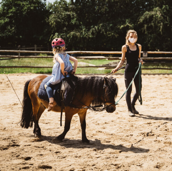 Reitlehrerin leitet ein kleines Mädchen, das rückwärts auf einem Pony reitet im Familienhotel mit Bauernhof