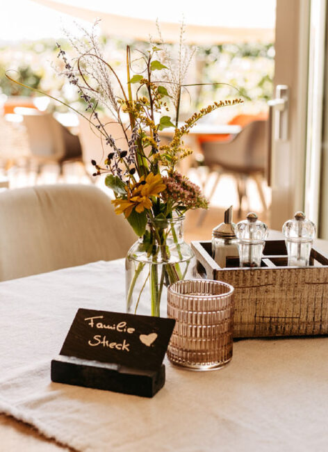 Vorbereiteter Tisch mit Blumenvase, Salz und Pfeffer und einer Platzkarte mit Namen im Familienhotel mit Bauernhof