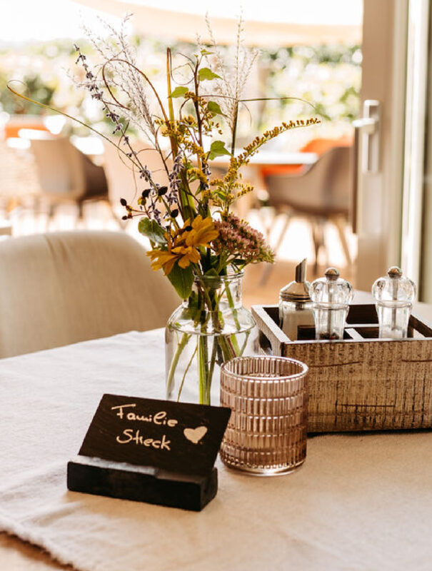 Vorbereiteter Tisch mit Blumenvase, Salz und Pfeffer und einer Platzkarte mit Namen im Familienhotel mit Bauernhof
