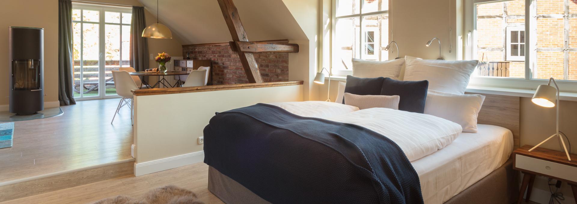 Einblick in das Zimmer im Landhaus Averbeck mit gemütlichen Bett , Kamin und einem Esstisch mit vier Stühlen